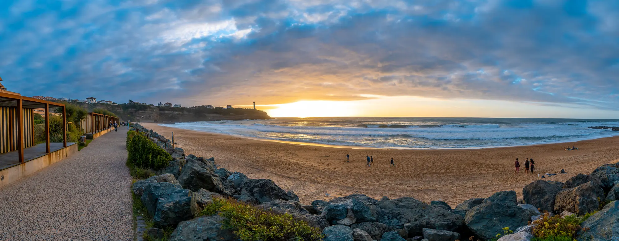 Beach and coastline at sunset, people walking on the sand and a cloudy sky over the ocean