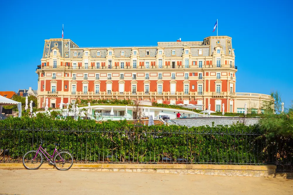 Façade of a grand hotel in red brick and pale stone, behind railings and a bicycle leaning against a low wall