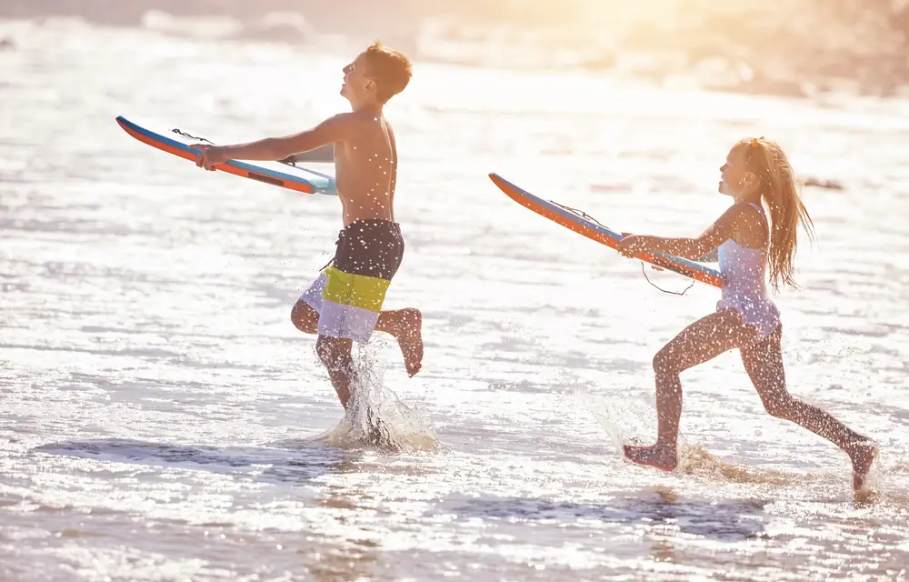 Two children run through the surf carrying their surfboards
