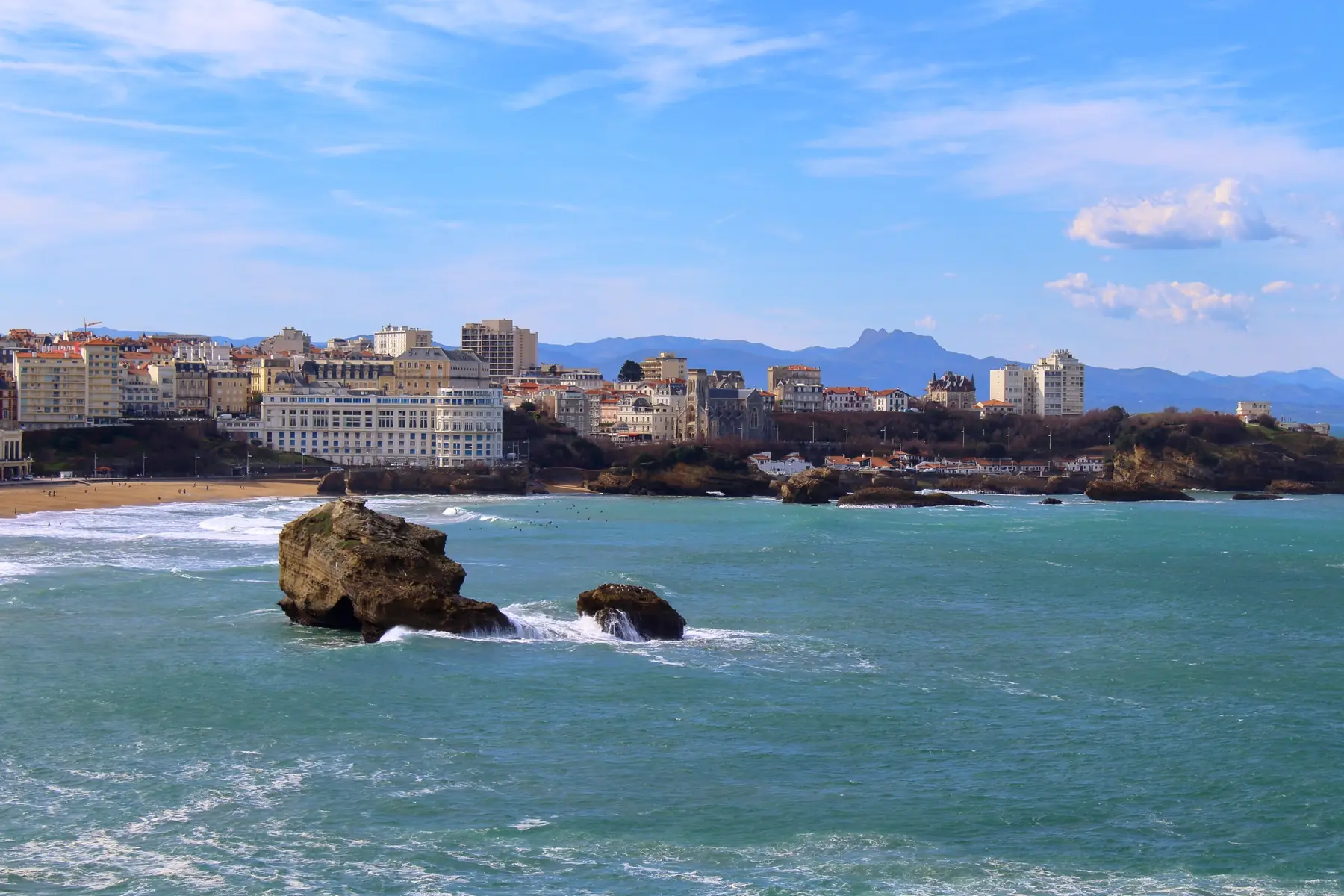 Seafront seen from the ocean, with buildings and villas on the cliff and mountains on the horizon